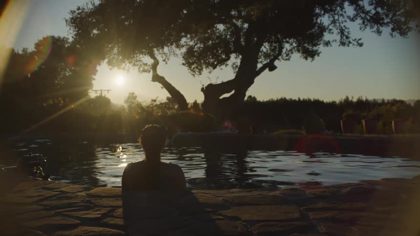 Woman sitting at a circular pool outdoors during sunset