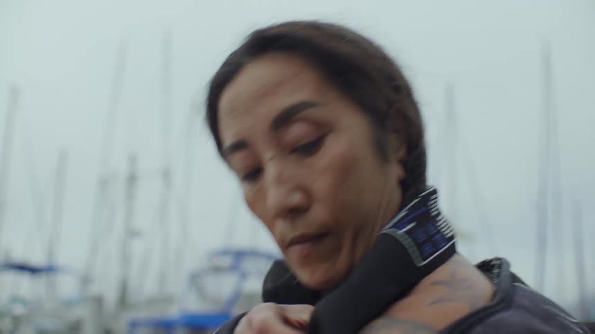 Portrait of a woman putting on and adjusting her wetsuit on a boat
