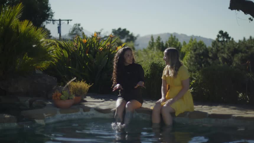 Two women talk beside a pool in a garden