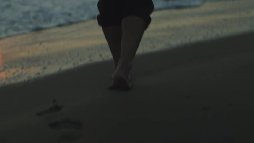 Woman walking across a beach at sunset leaving footprints in the sand