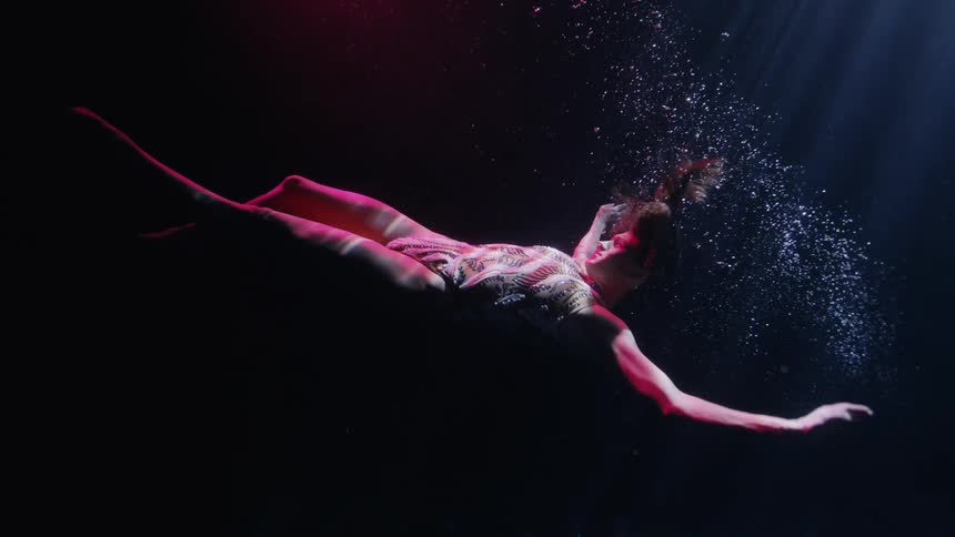A woman swims underwater in the dark