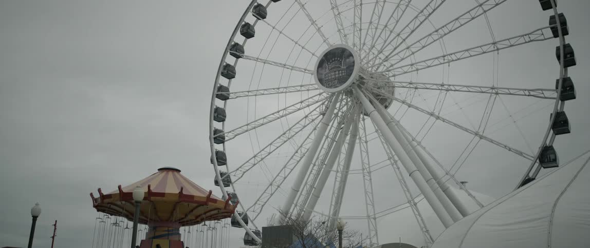 A large ferris wheel turning in a carnival on a cloudy day
