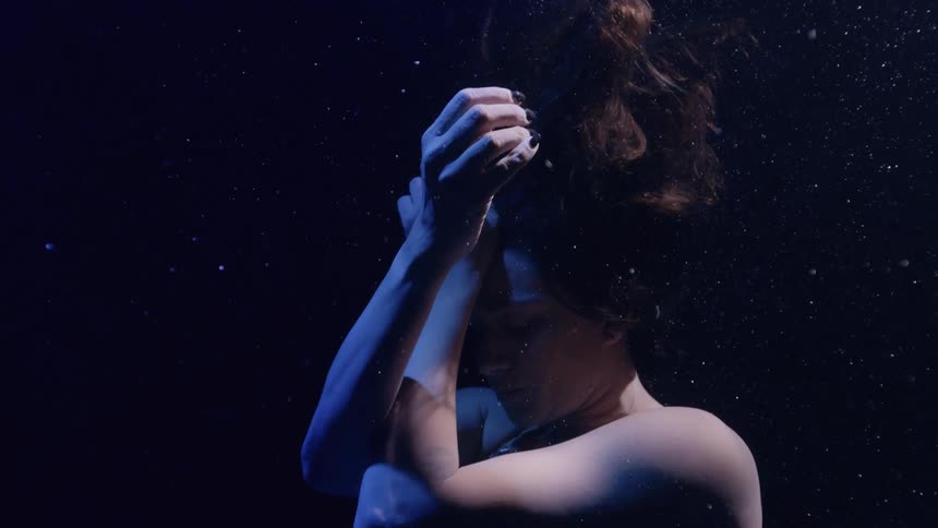 Woman floating underwater crosses her arms in front of her face