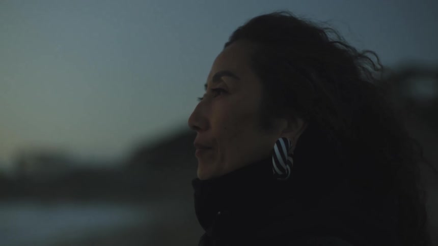 A woman stands still on the beach then steps toward the ocean at dusk
