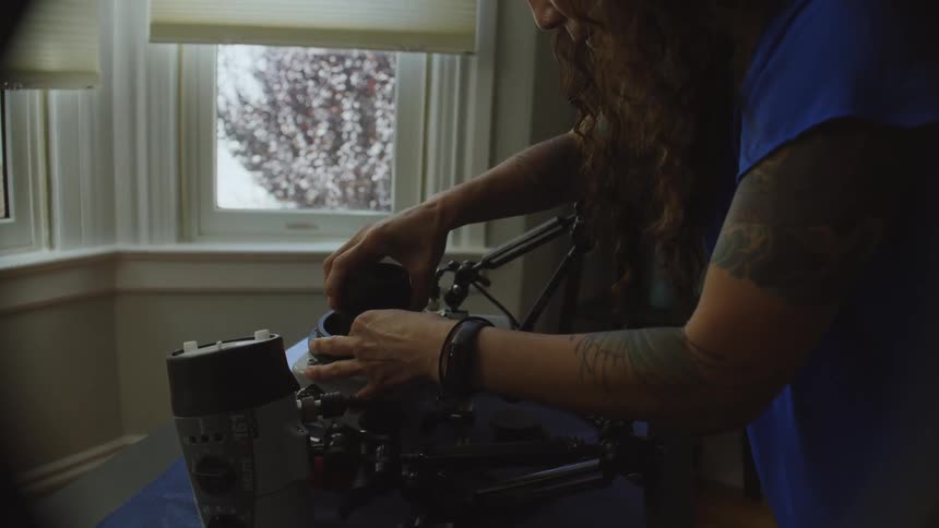 A woman is at home in a room setting up a complex camera housing in front of a window in the daytime