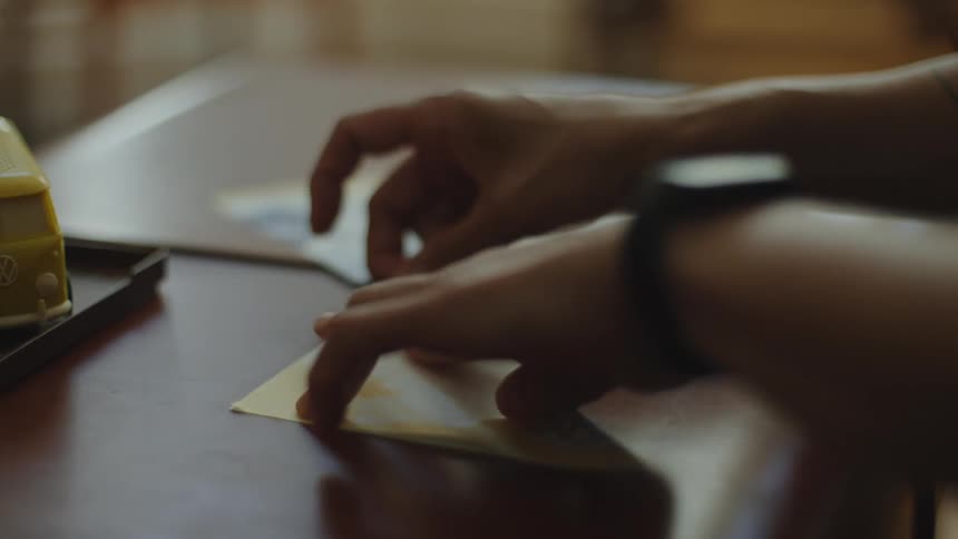 A woman's hands carefully fold and crease a square of origami paper