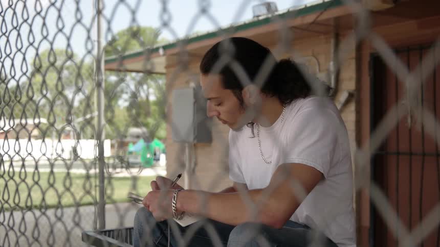 A man is sitting behind a fence writing