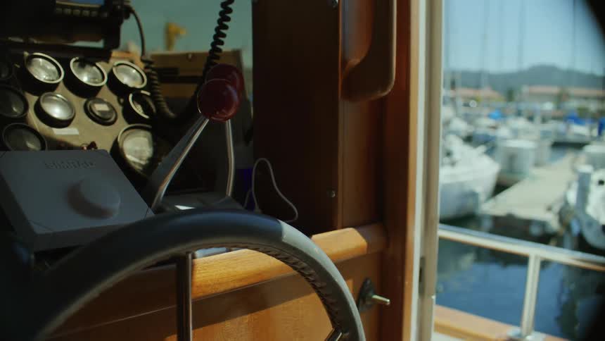 Dashboard on a boat next to a window showing other boats on the water and mountains on the background during day time