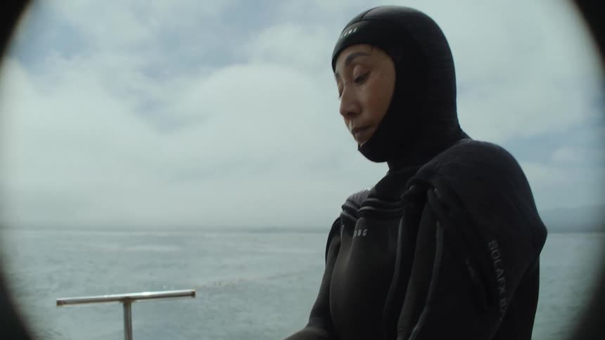 A woman in a diving suit puts on gloves on a boat on the water