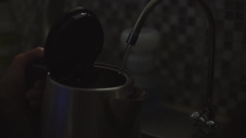 A person filling a container with water in the kitchen sink