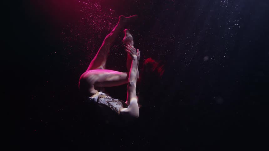Woman dancing gracefully in the pool with a colorful light reflecting on her