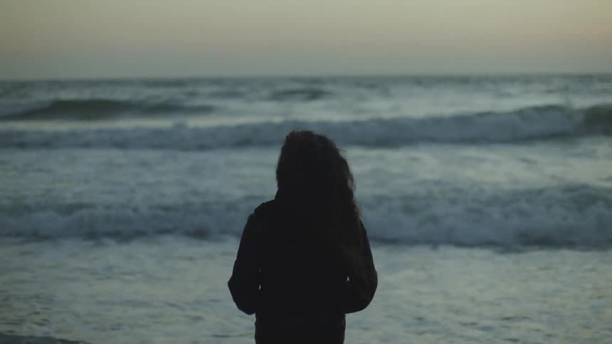 A silhouette of a person on the beach looking out to sea with waves crashing