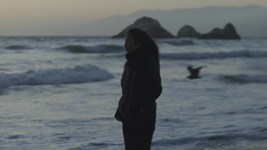 Thoughtful woman wearing a jacket walking along a beach on a windy day