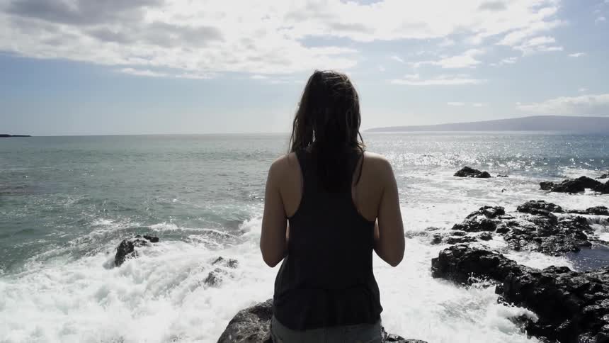 A woman stands before waves crashing on rocks