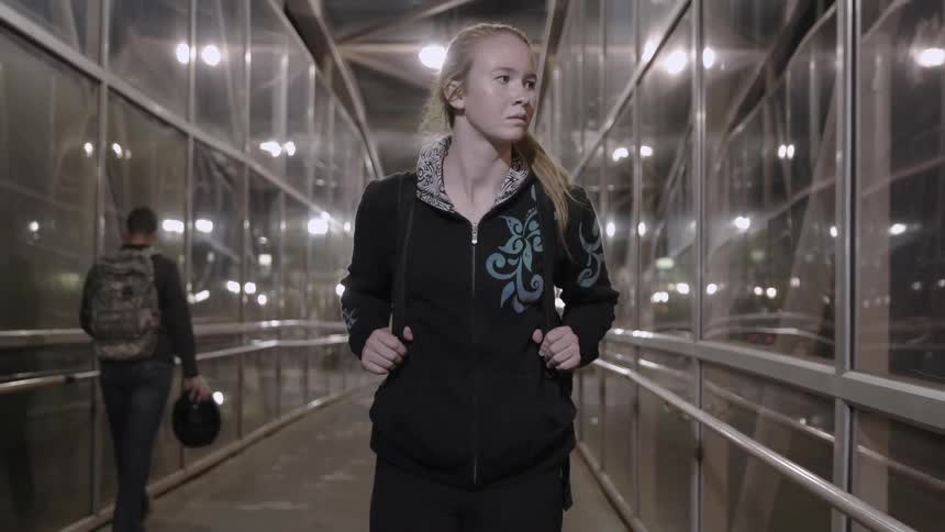 A woman is walking down a long hall at night