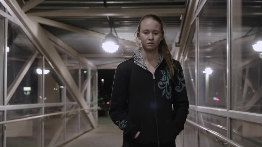 A girl is walking through a glass overpass at night