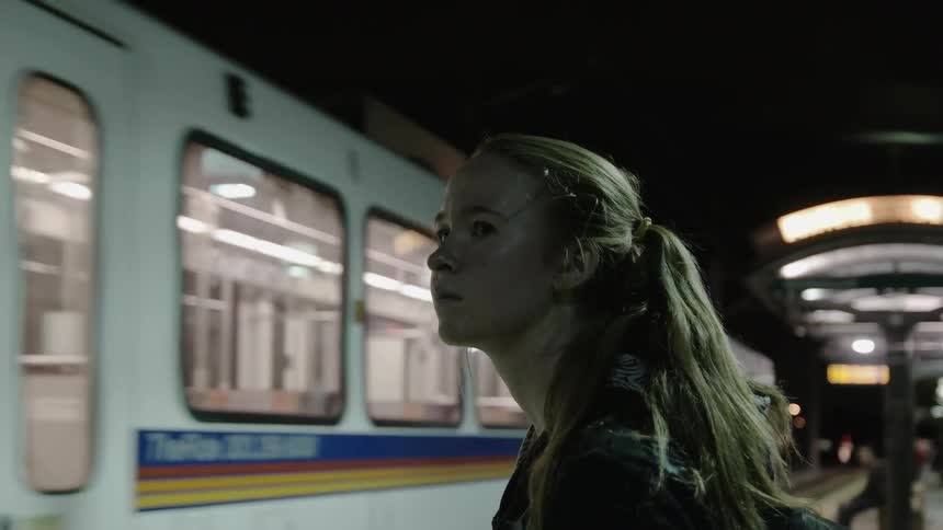 A girl stands and waits while a subway train drives by
