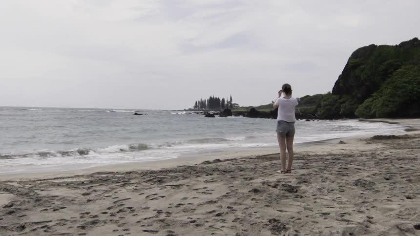 A woman is standing on the sand of a beach