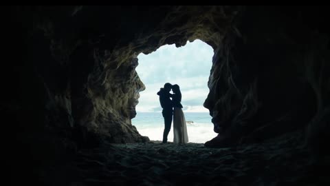 A man and women hug near the foot of a cave by the beach