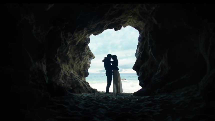 A man and women hug near the foot of a cave by the beach