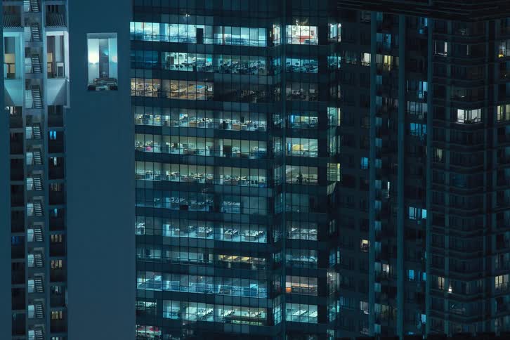 The exterior view captures an office in the city at night with lights flickering highlighting the bustling and dynamic nature of urban workspaces
