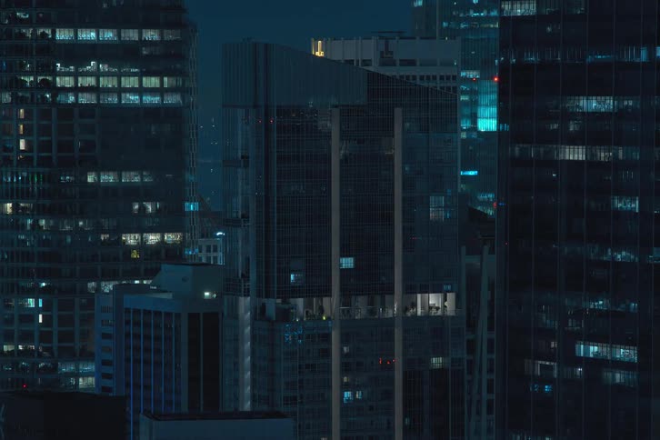 Exterior view of tall residential and office buildings with flickering lights turning off during night in the city