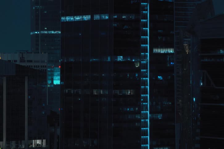 Blue reflected lights flicker through skyscraper windows before turning off and going dark at night
