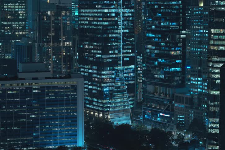 An area with several tall buildings and apartment lights that turn on quickly