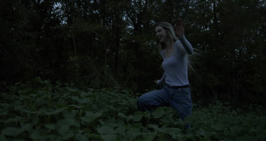 A blonde woman dressed in a white shirt and jeans joyfully runs through the forest embracing the freedom and serenity of nature