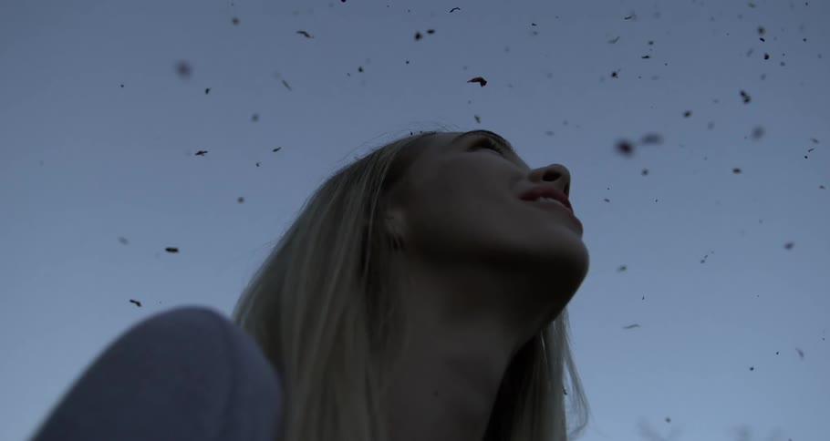 A young blonde woman is looking at the sky while several particles are falling