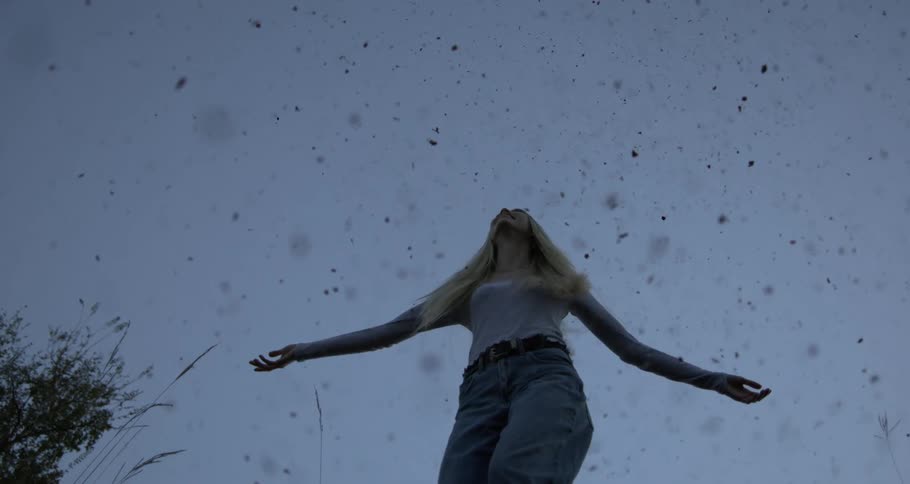 Upward view of a woman with arms open in a clear sky while it snows in slow motion
