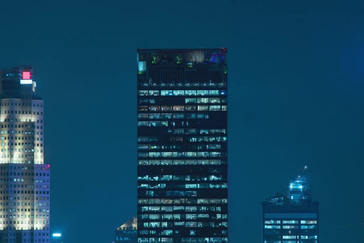 Blue reflected lights turning on and off through skyscraper windows in the city at night against a dark blue sky