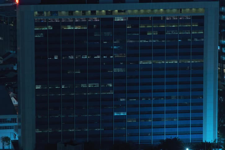 The exterior view captures an office in the city at night with lights flickering highlighting the bustling and dynamic nature of urban workspaces