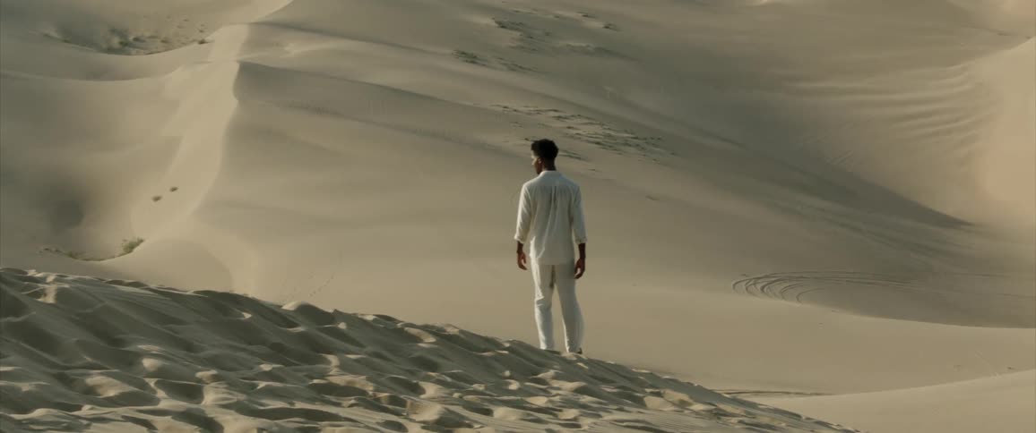 Man in allwhite clothing walking through the desert dunes