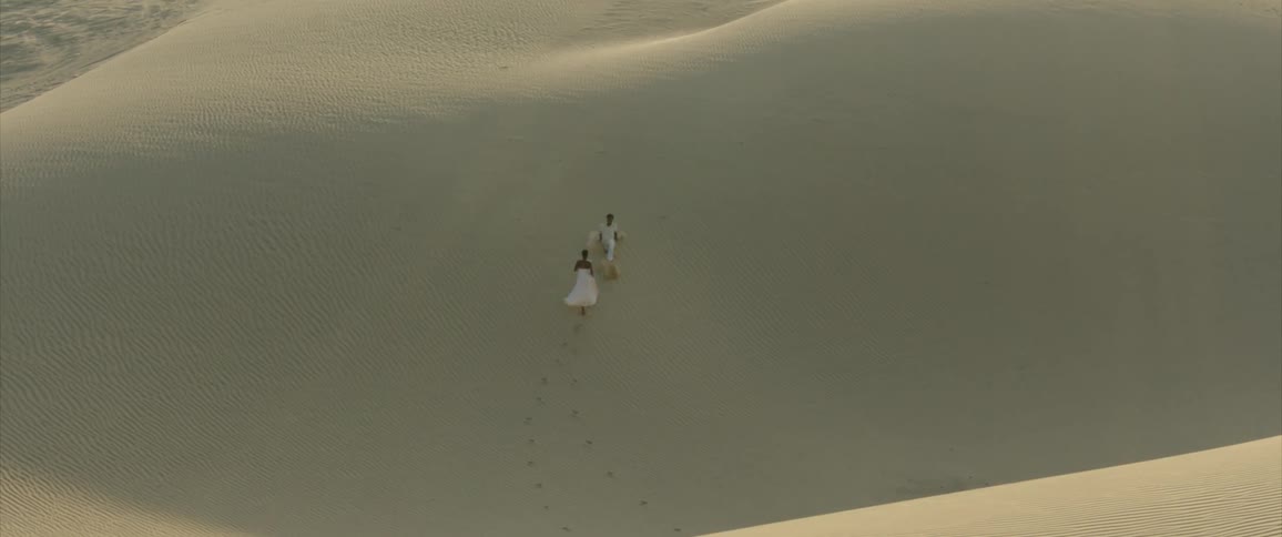 Couple running up a sand dune in the desert
