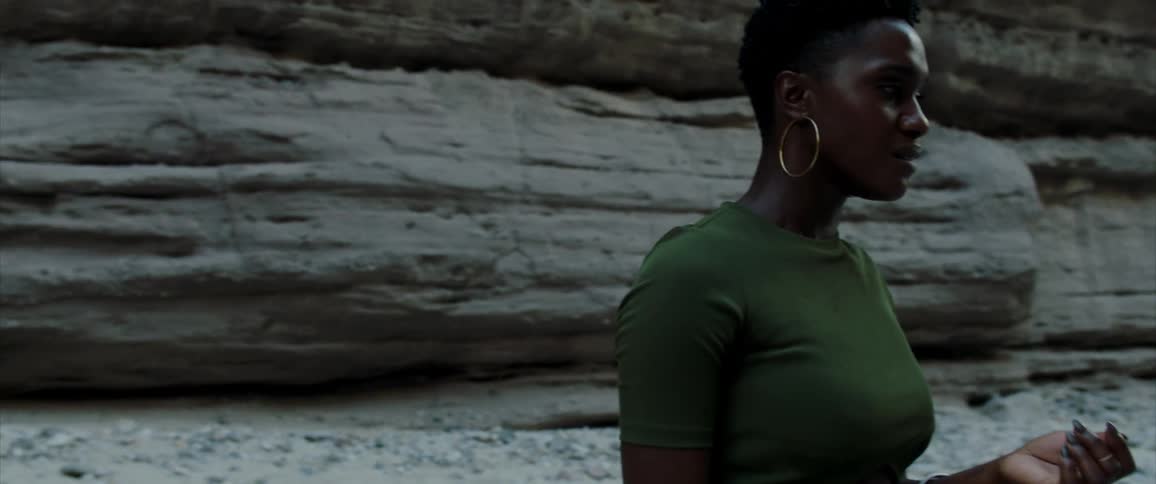 A woman with hoop earrings stands next to a rock