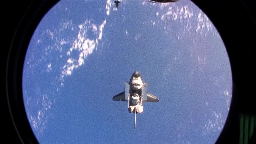 A space shuttle turns upward as it flies over the earth