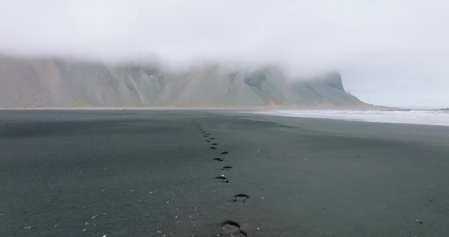Footprints on a black sand beach near the sea with high mountains in the background