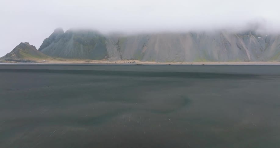 A region of a sea landscape and behind a huge mountain between clouds in the sky