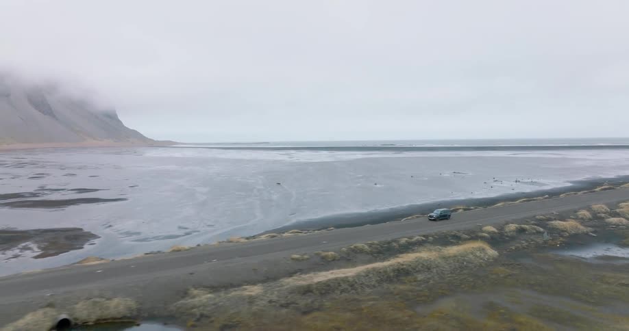 Suv driving on a natural road amid a sea and a chain of mountains