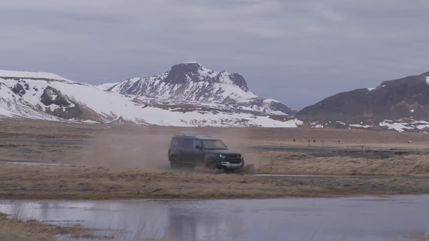 A car passes through a puddle of water and makes a splash and behind it is a mountain with snow