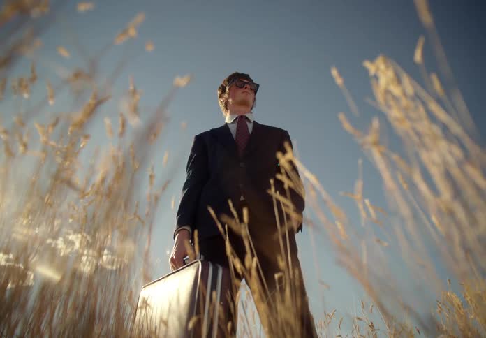 A man wearing a suit and sunglasses in a field during a hot day