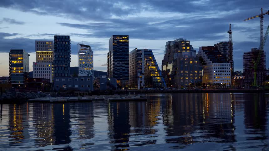 A vibrant cityscape at dusk with its lights reflecting in the still waters of the harbor