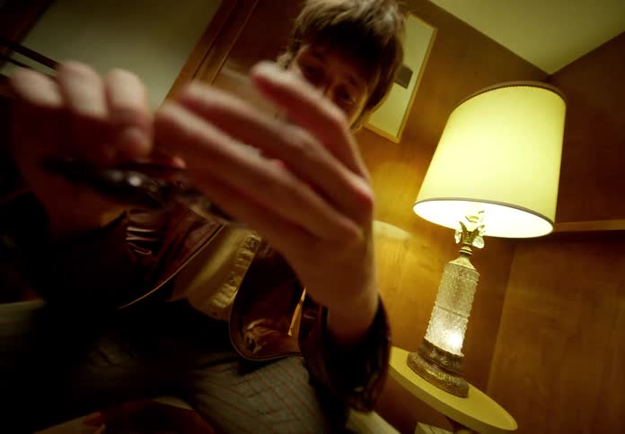 Man sits indoors removes glasses and puts them in jacket pocket