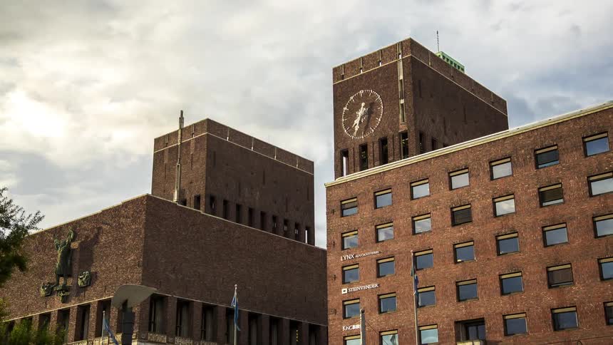 Pedestrians move along street next to architecturally similar buildings as hands on external clock advance