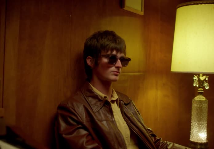 Man sitting next to a piano and putting on sunglasses