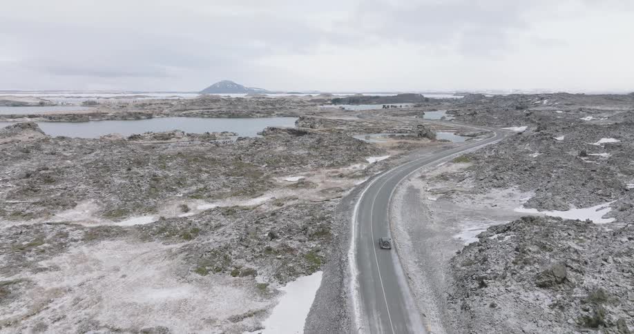 Aerial of a car on a deserted road between mountains and lakes