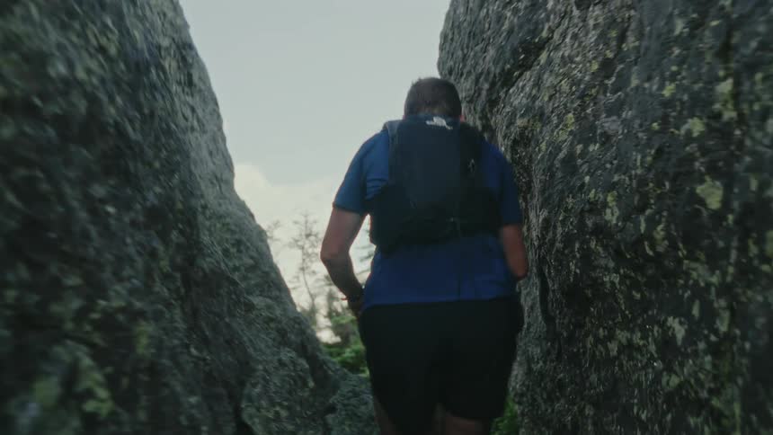 A man wearing a small backpack hikes quickly through a rocky pass