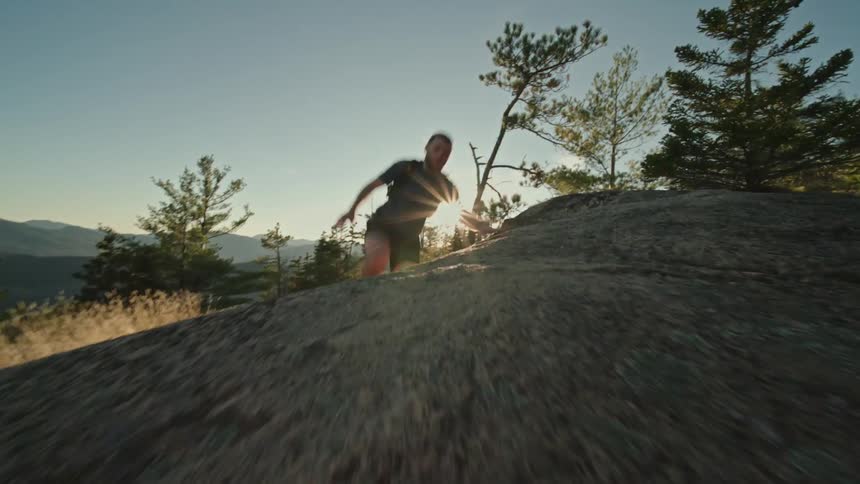 View of a man jumping and running along a trail in the mountains with the sun setting on the horizon