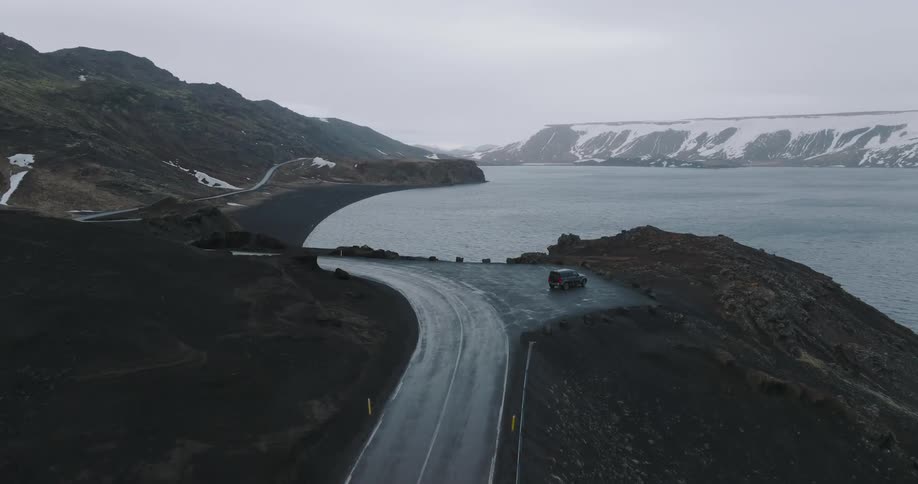 Aerial view of a road through the mountains with a lake beside it